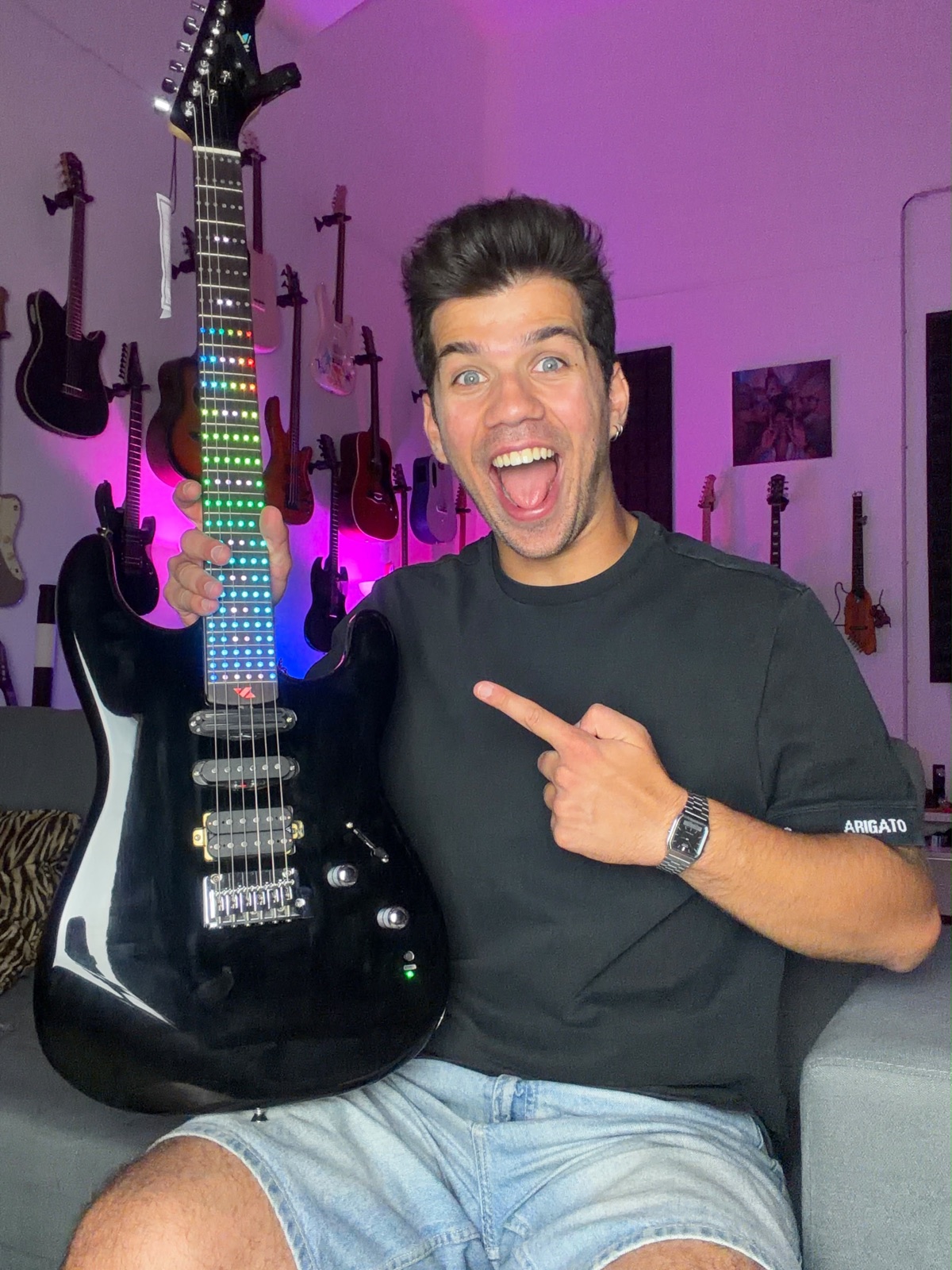 Alex Vale sorrindo e apontando para a guitarra de LED